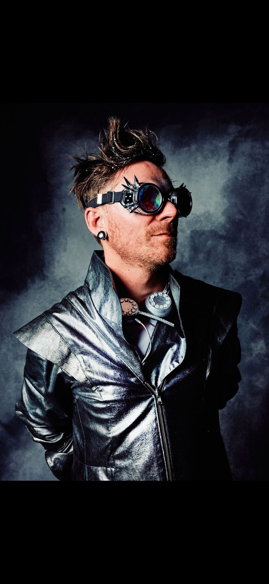 Spif portrait — silver chrome jacket, futurist goggles with prismatic lenses, spiked hair, telephone-rotary necklace, smoky studio backdrop