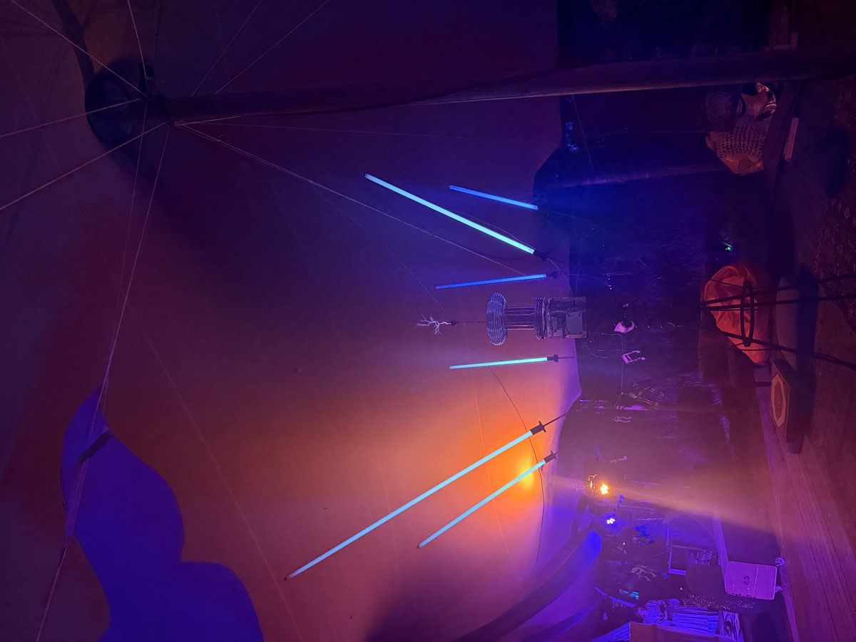 Glowing tubes fan out from the coil like spokes against the dark tent, orange glow beyond