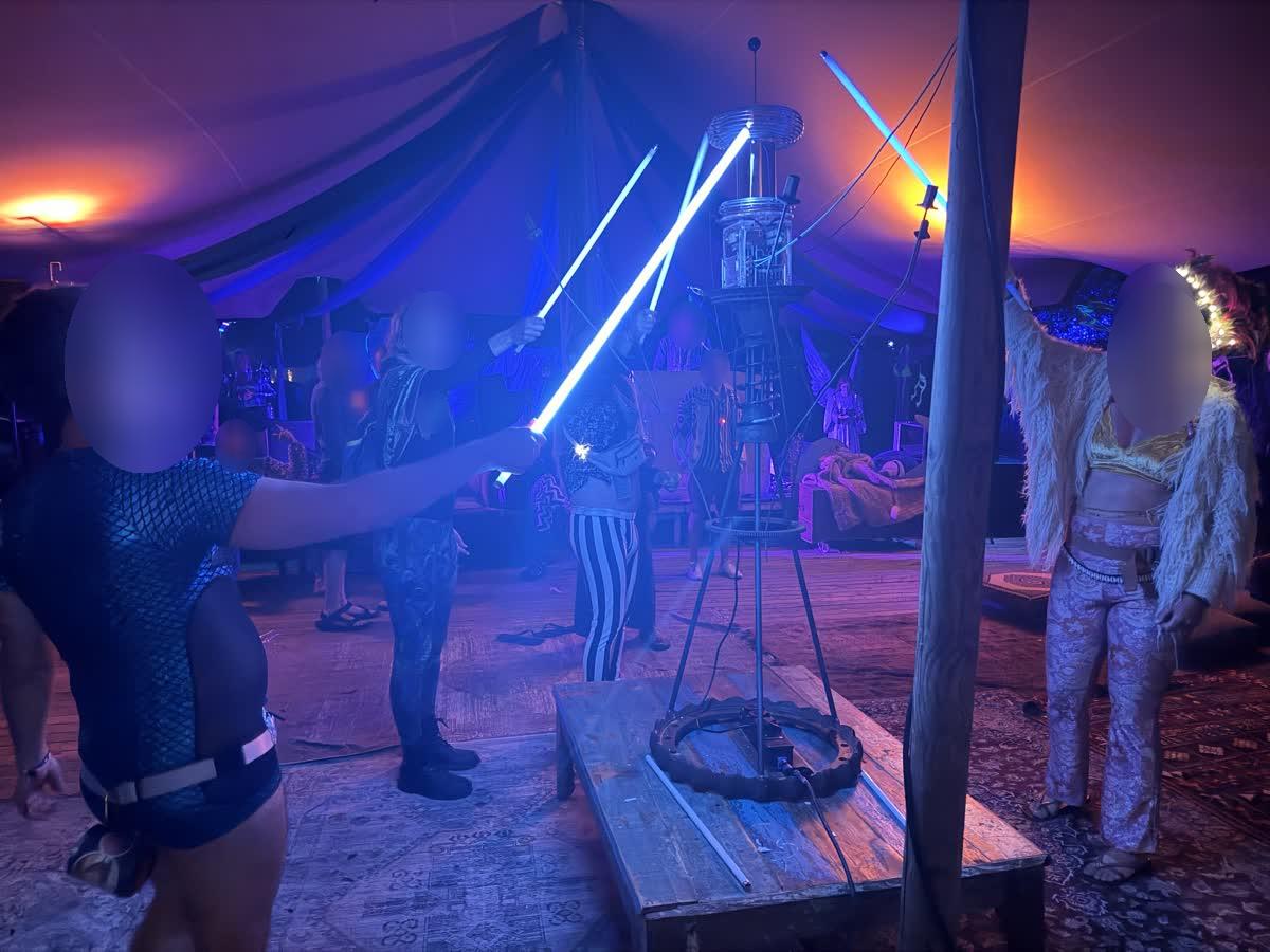 People cross glowing blue tubes at the coil, forming a star of light in the tent