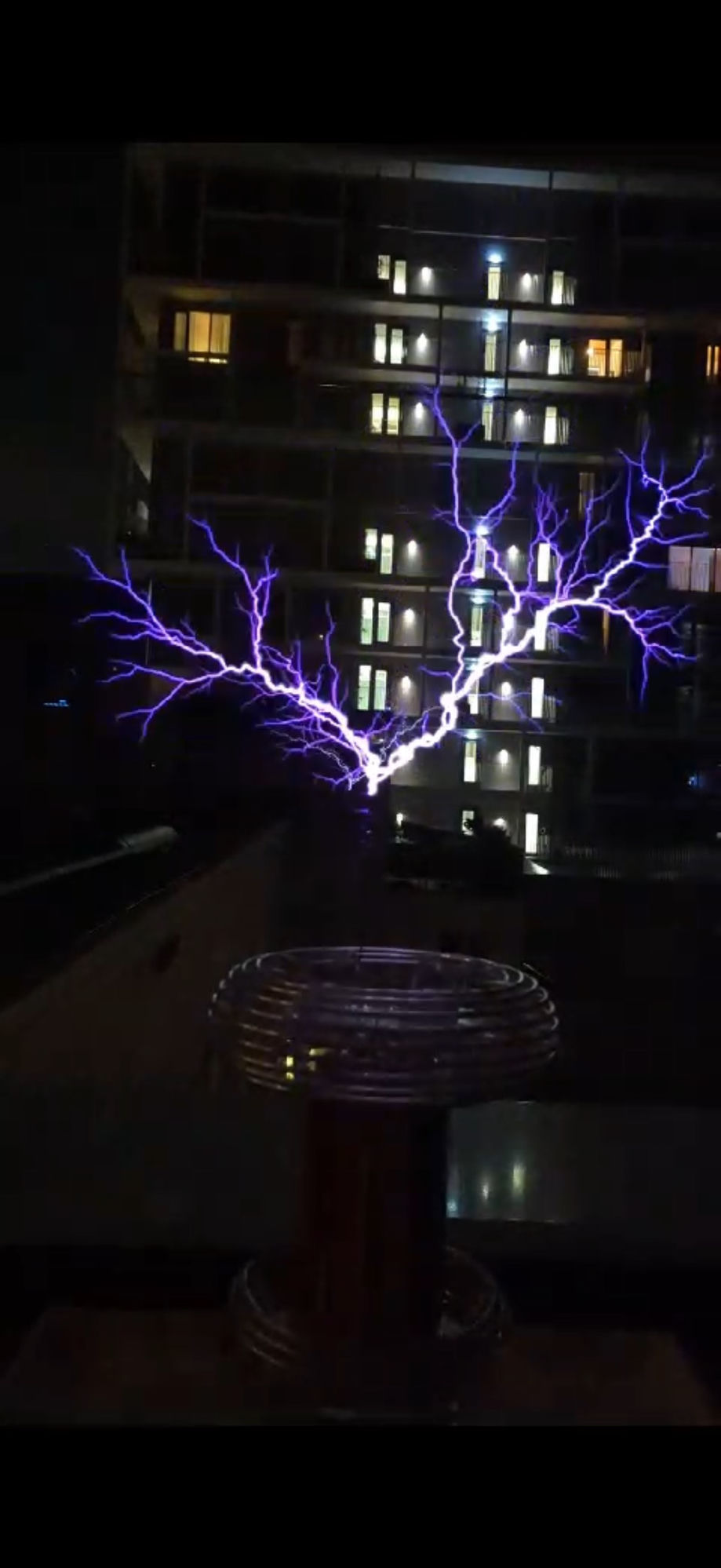 Tesla coil mid-discharge with branching purple arcs against an Amsterdam apartment building at night